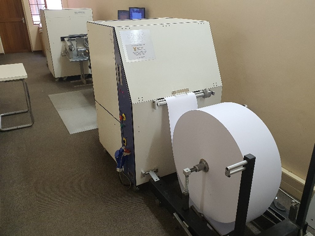 A machine with a large roll of paper feeding into it. This machine is used to produce braille documents in bulk!