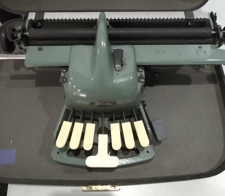 Blista Braille Type writer, a green machine with a mechanism of y keys to type braille which slides over the paper insert tray.