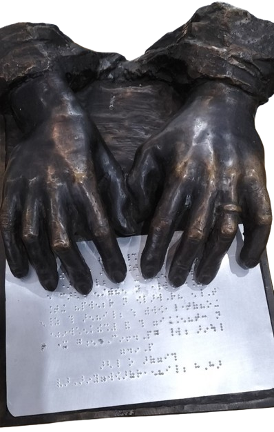 A bronze artwork of 2 hands feeling a metal plate embossed with braille.